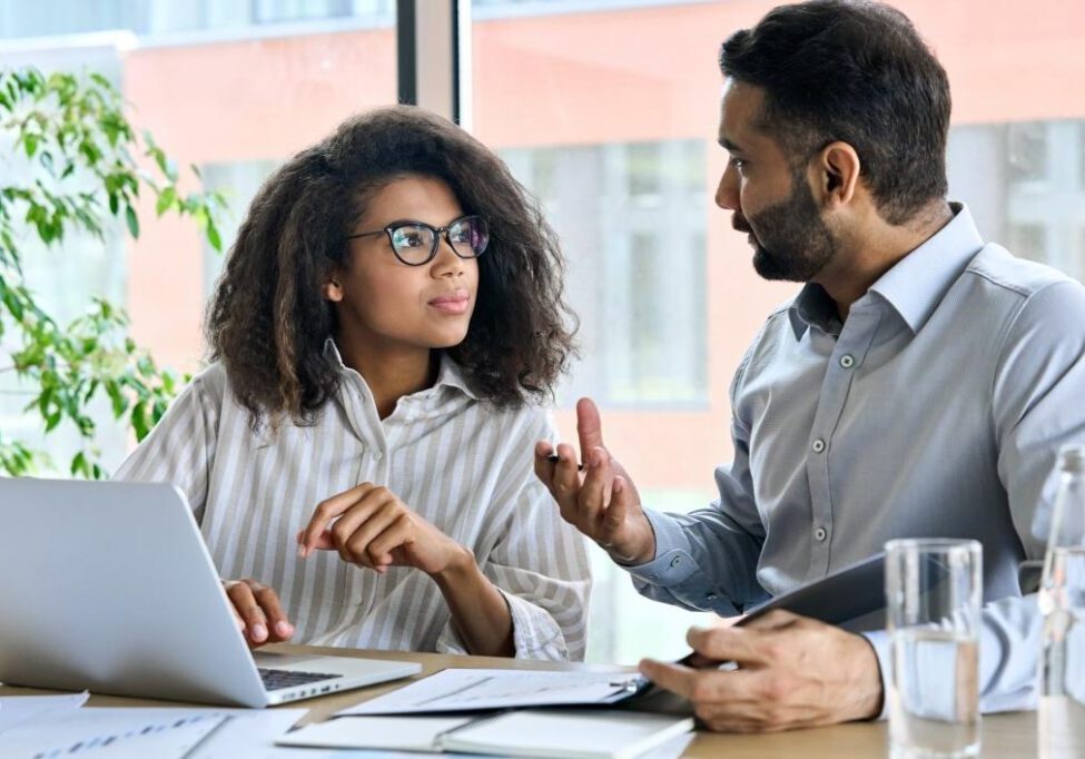 Two colleagues discussing work at a desk.